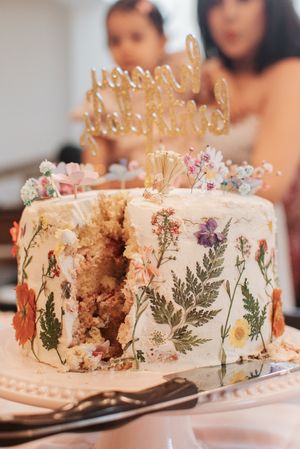 Sliced birthday cake showing layers decorated with pressed flowers and gold topper.