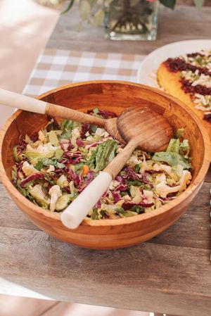 Colorful mixed salad with wooden serving utensils in rustic wooden bowls.
