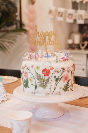 Elegant birthday cake decorated with pressed flowers and a gold Happy Birthday topper.