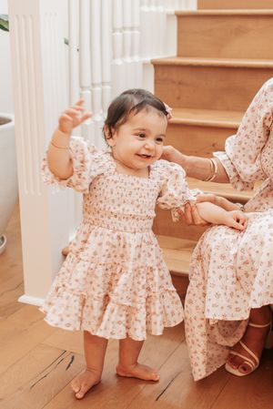 Child in pink floral dress exploring and playing around white staircase and wooden floor.