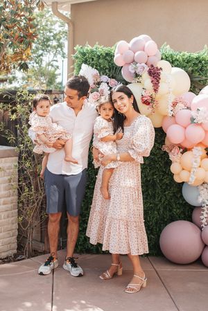 Outdoor family photo against green hedge with elegant pink and peach balloon arch decorations.