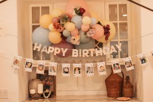 Happy Birthday banner with photo timeline and pastel balloon arch decorations against white doors.