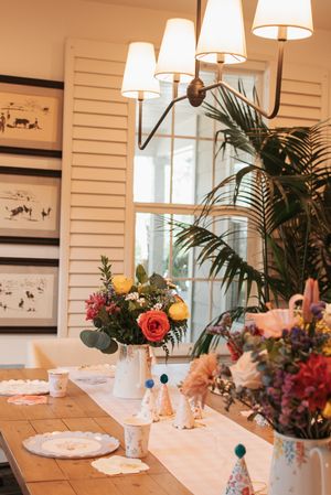Elegant dining table setting with floral arrangements, white lamp chandelier, and palm plants.