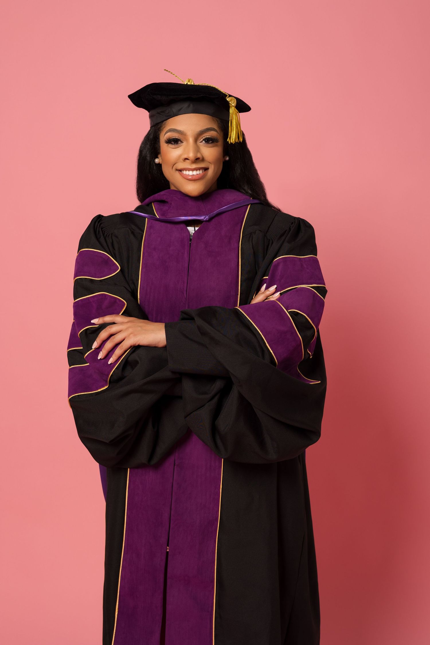 Graduation portrait in traditional black and purple doctoral regalia with gold tassel.