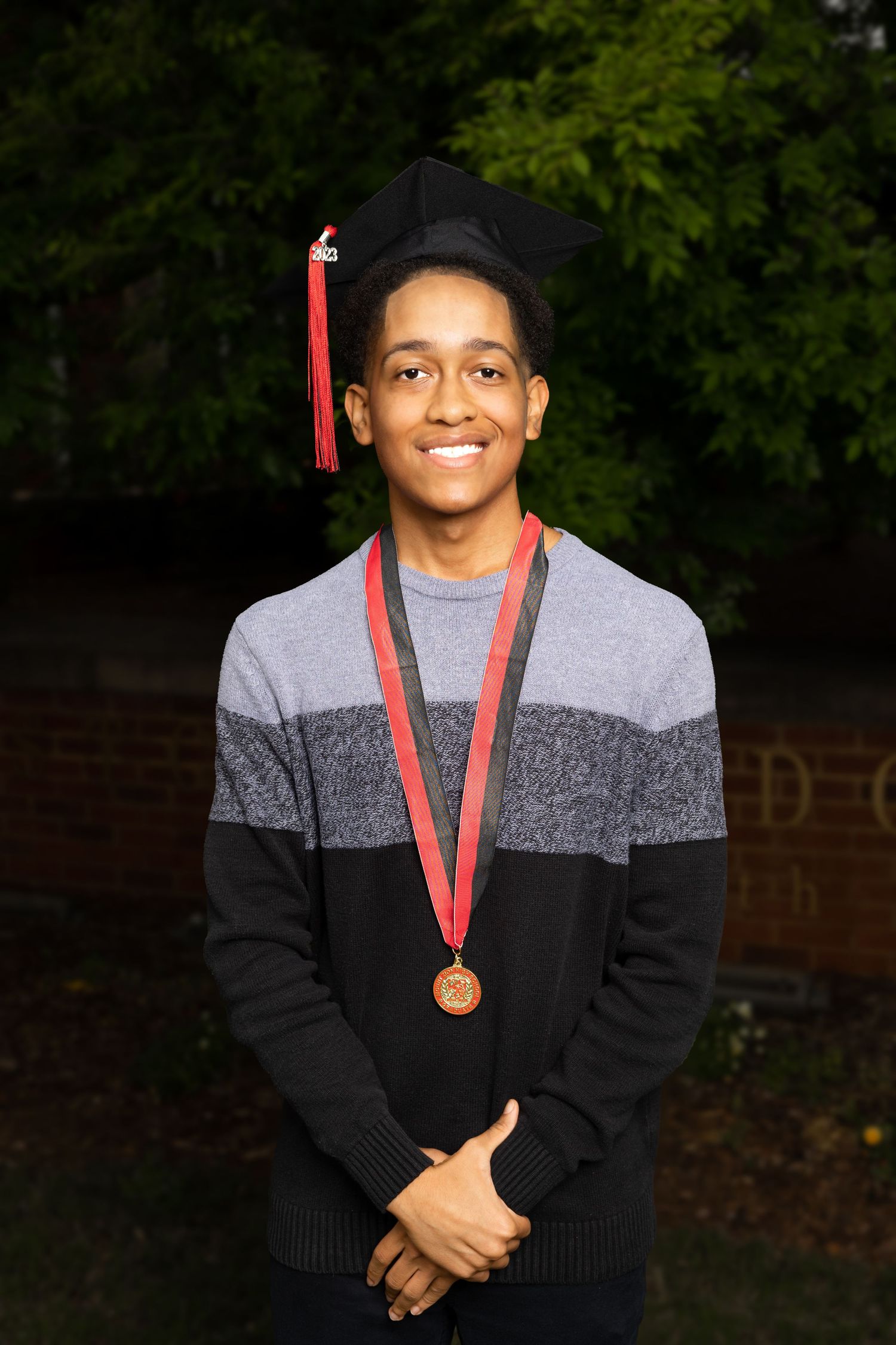 Graduate wearing graduation cap and medal poses in striped sweater.
