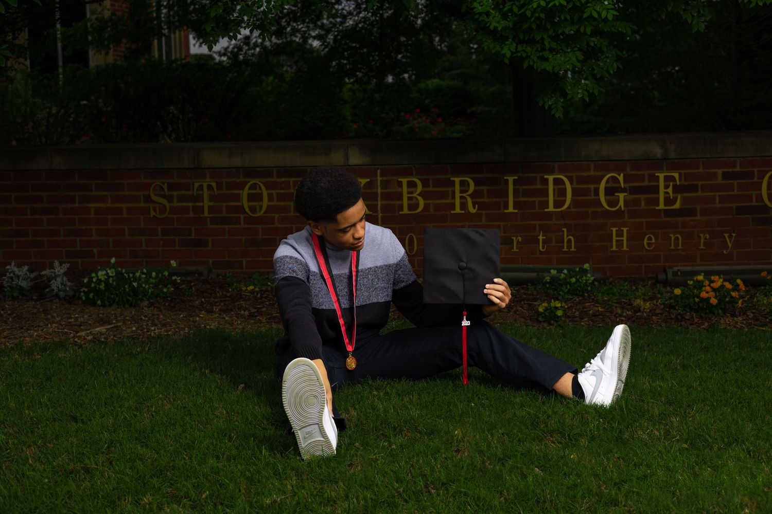 Graduate relaxes on grass near brick wall during photo session.