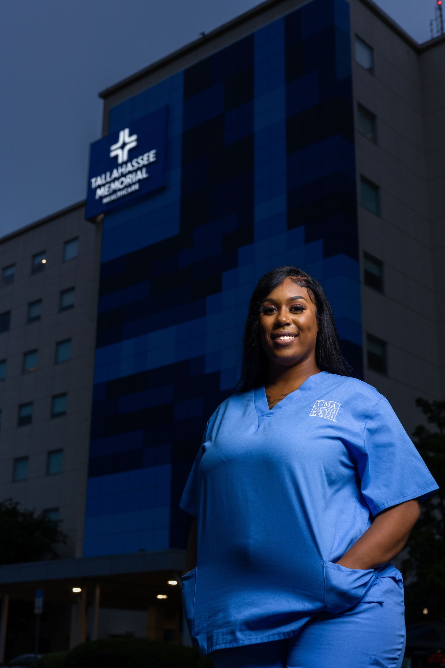 Healthcare worker in blue scrubs standing outside medical facility at dusk.