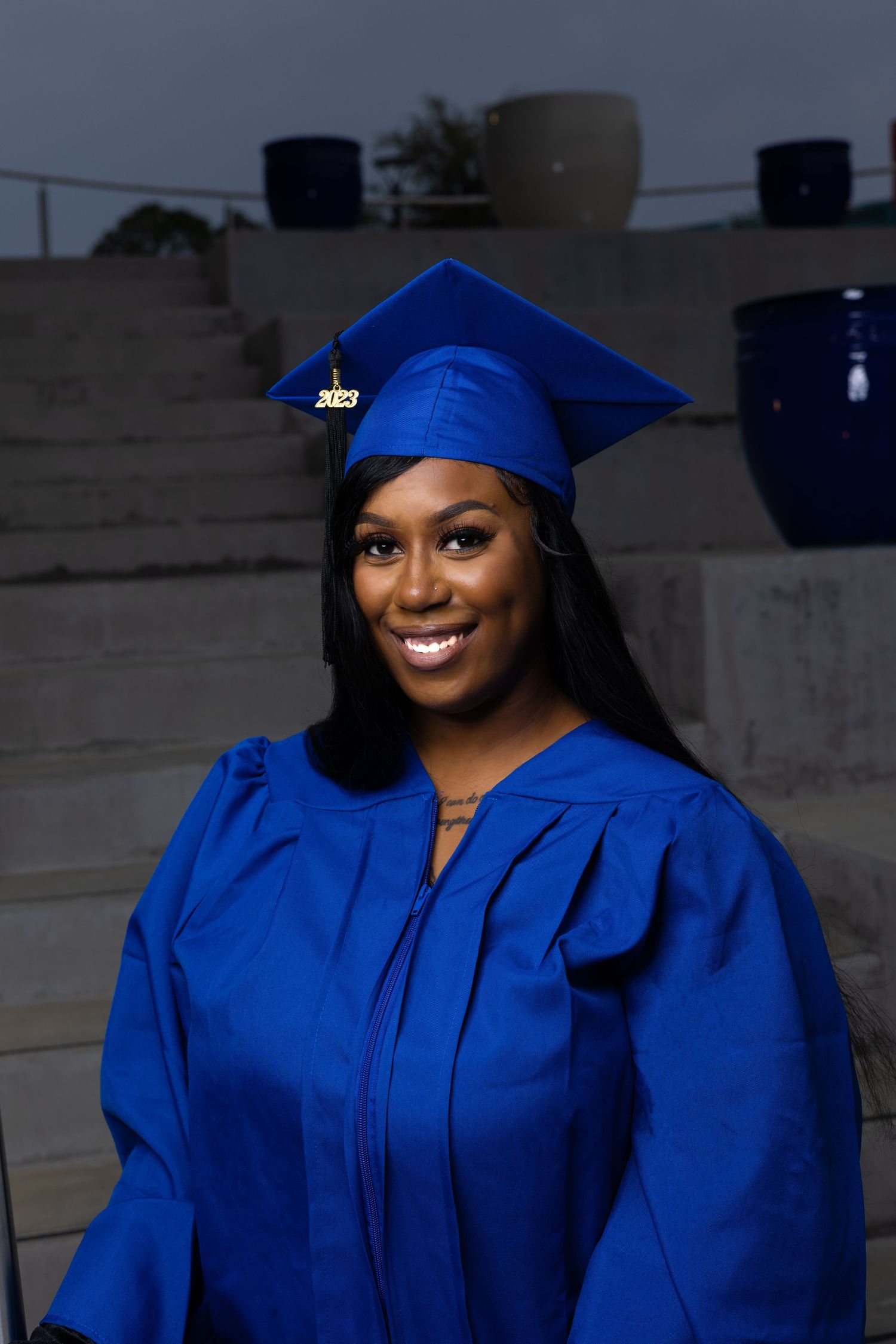 Graduate wearing royal blue graduation gown posing outdoors at dusk.