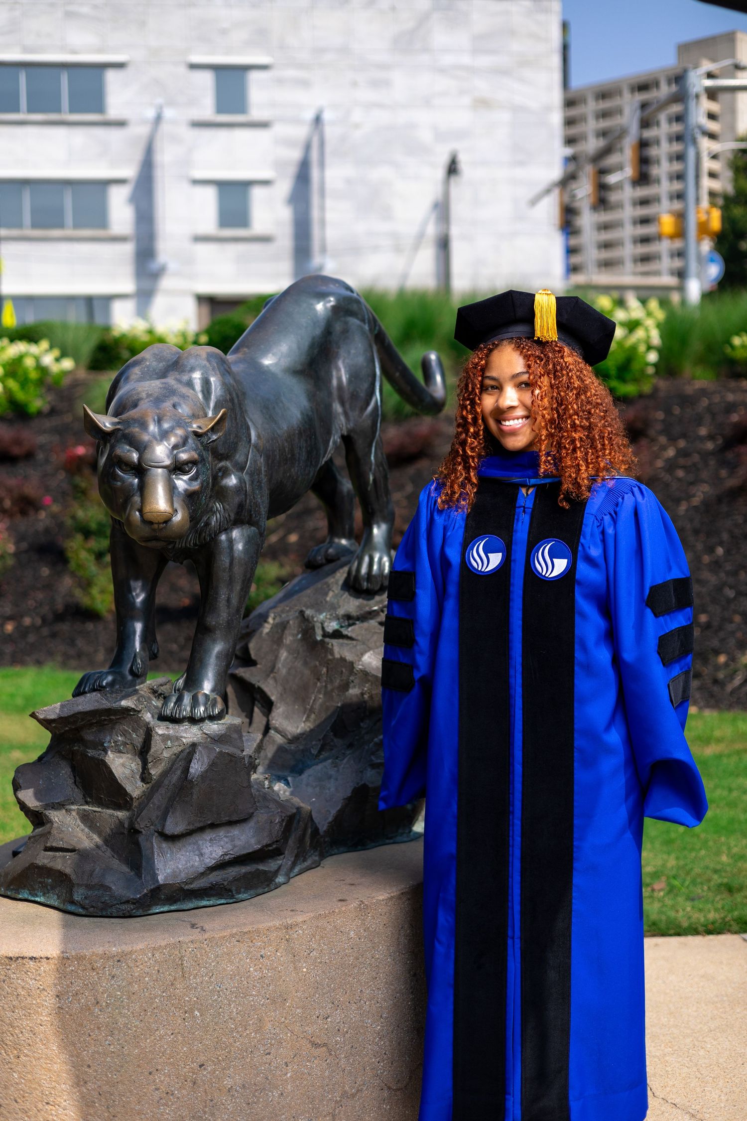 A graduate poses with GSU's iconic black panther statue wearing doctoral robes.