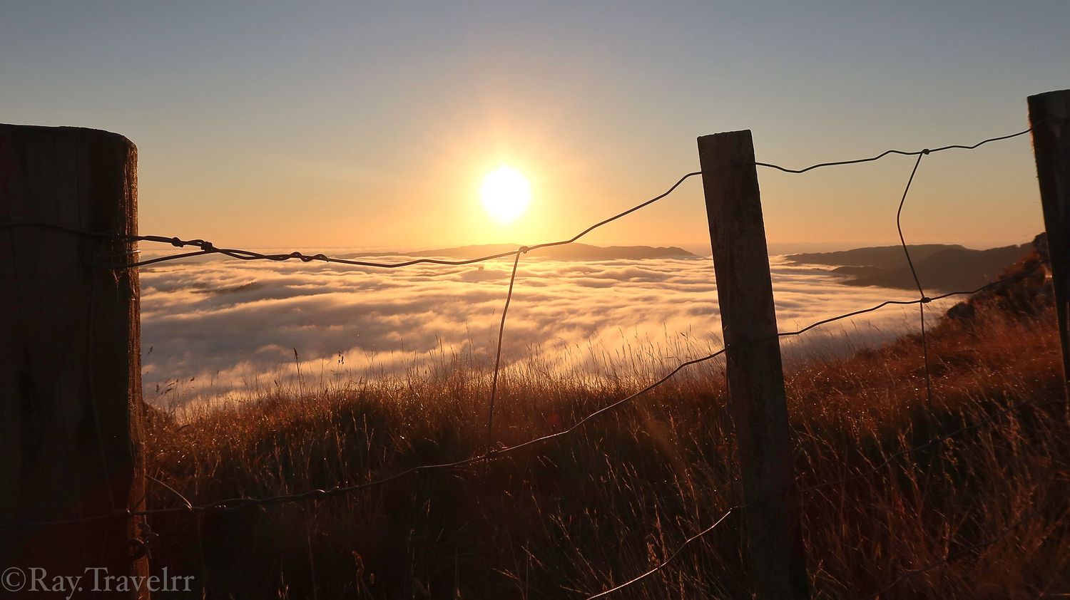 Golden sunset over foggy valley with silhouetted fence posts in foreground.