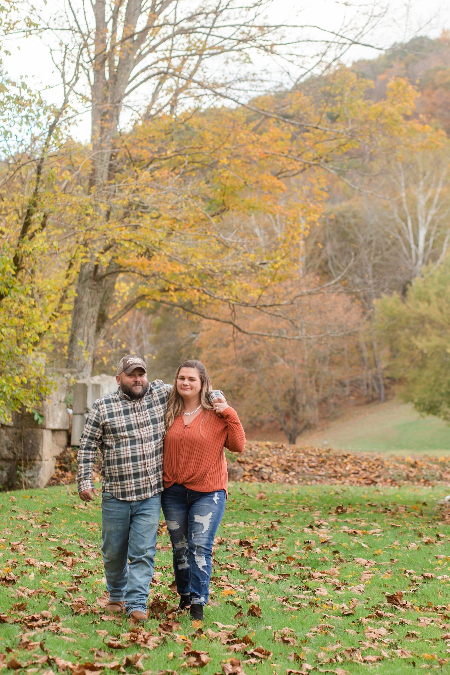 Couple walking through fallen leaves in an autumn landscape with golden trees.