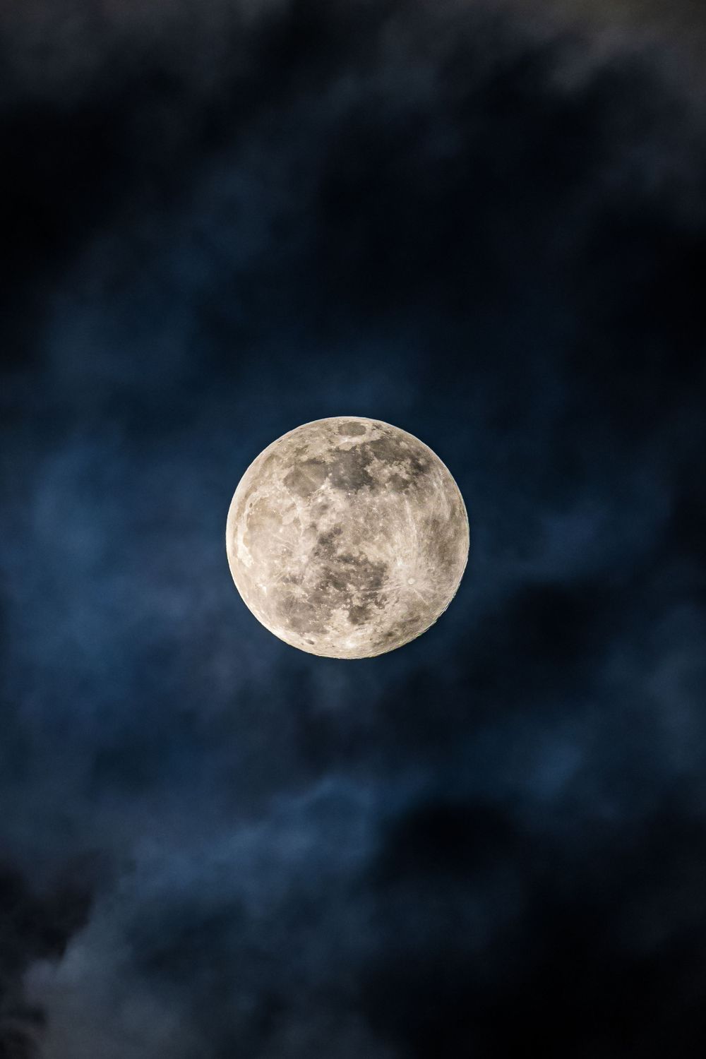 Full moon in crisp detail against a dark blue cloudy night sky.