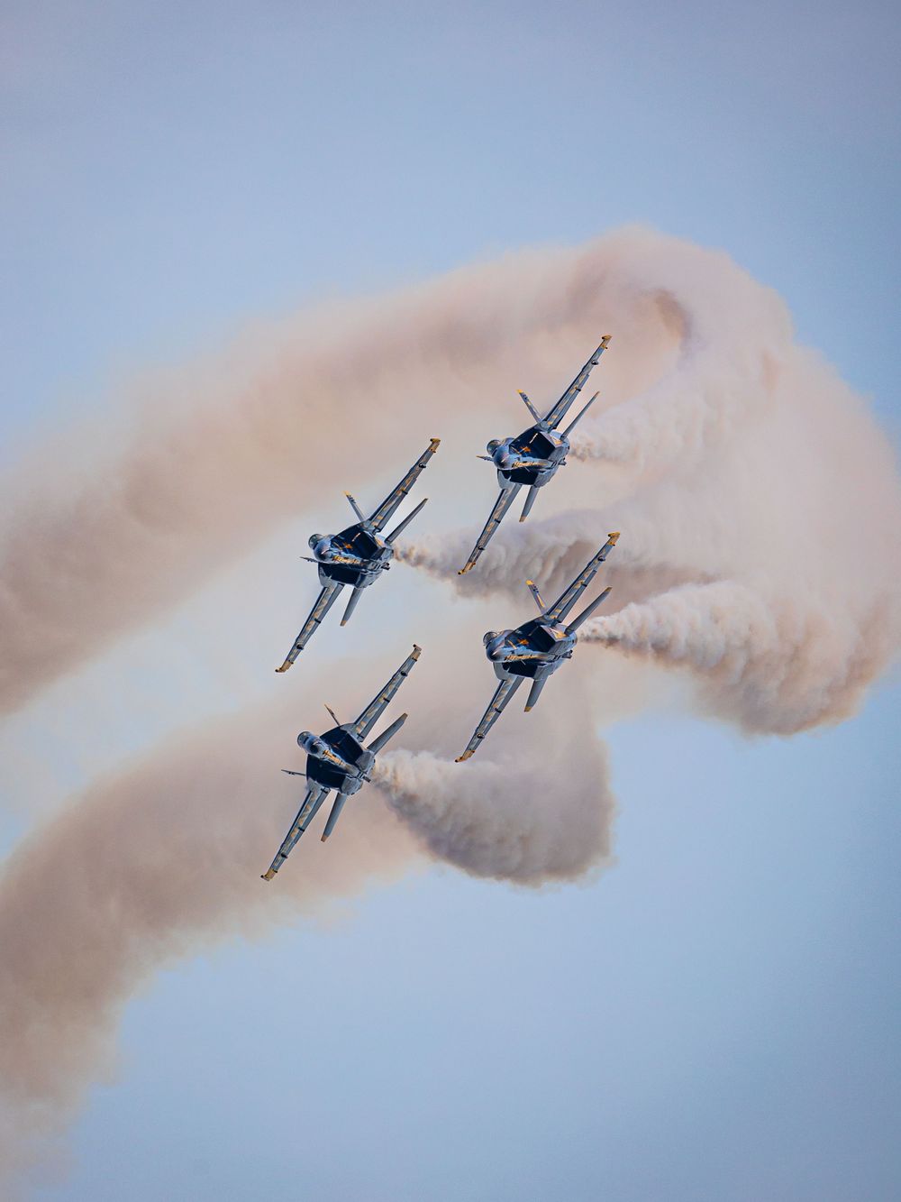 Four military jets performing an aerobatic display with trailing smoke against blue sky.
