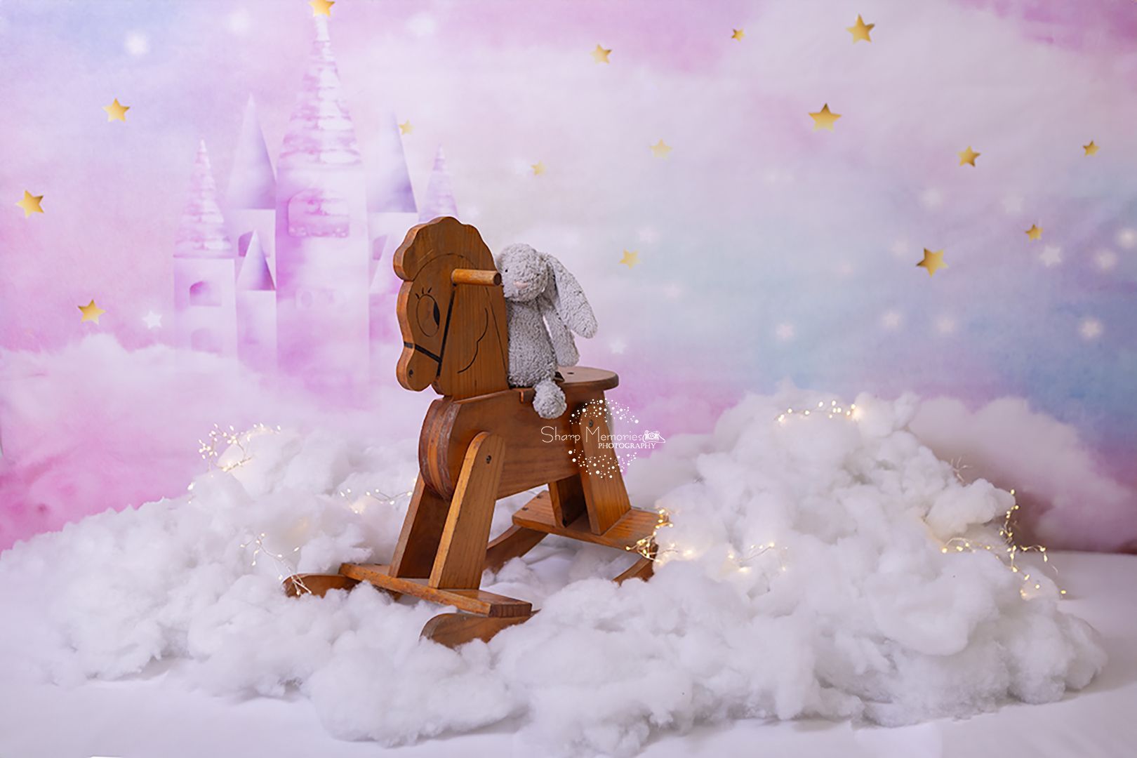 A wooden rocking horse toy sits in cotton clouds under a dreamy pink sky with twinkling gold stars.
