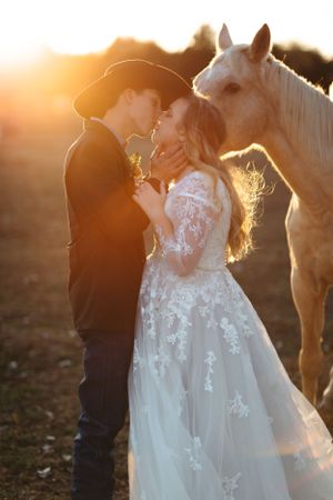 A romantic wedding photo with a white horse joining the couple during a golden sunset moment.