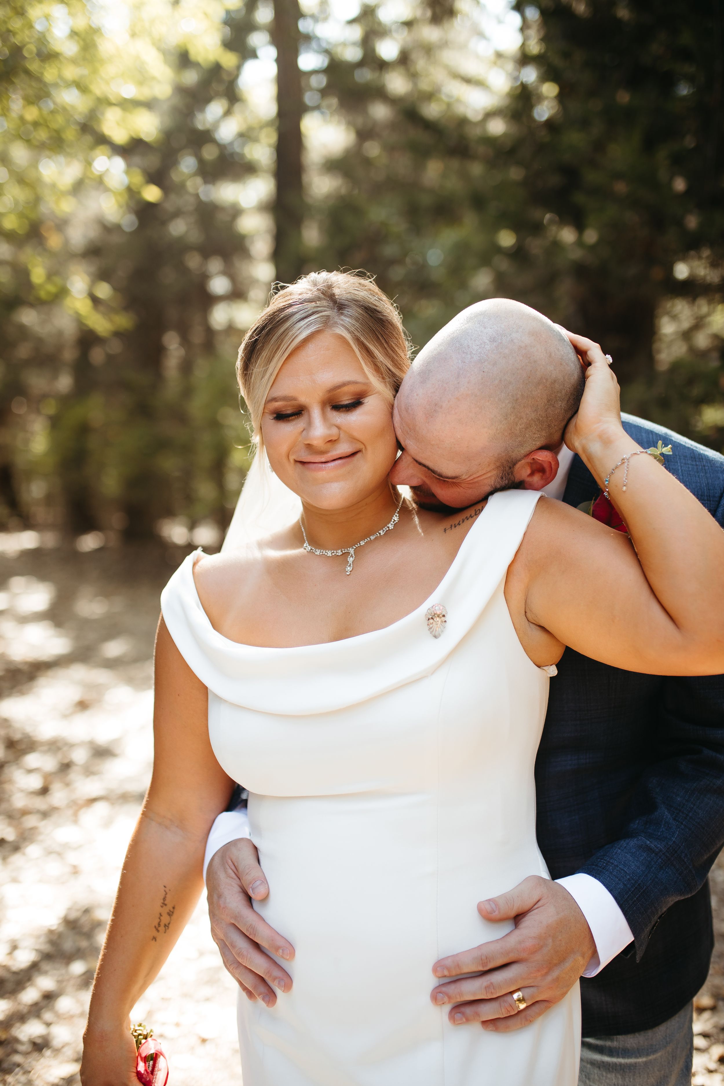 Intimate moment between newlyweds in sunlit forest setting.