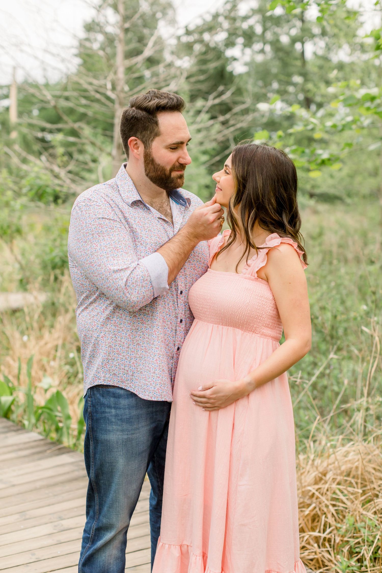 A romantic maternity portrait of a couple sharing a tender moment on a wooden path.
