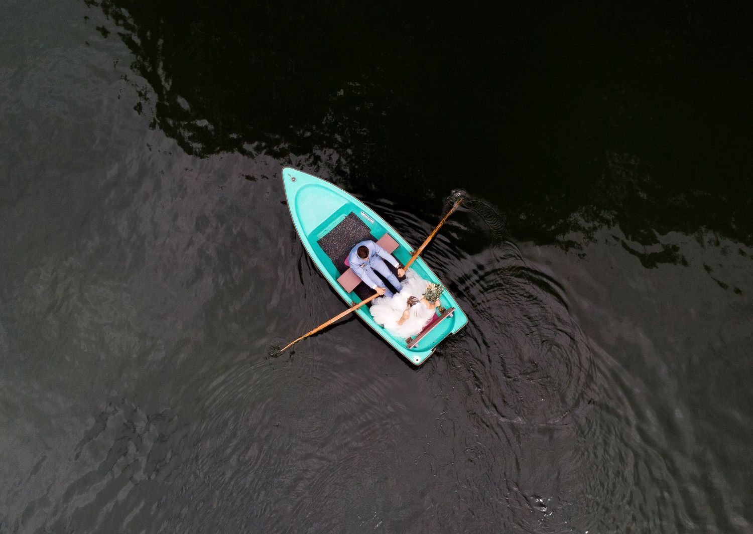 Turquoise boat floating on dark water captured from above with rippling reflections.