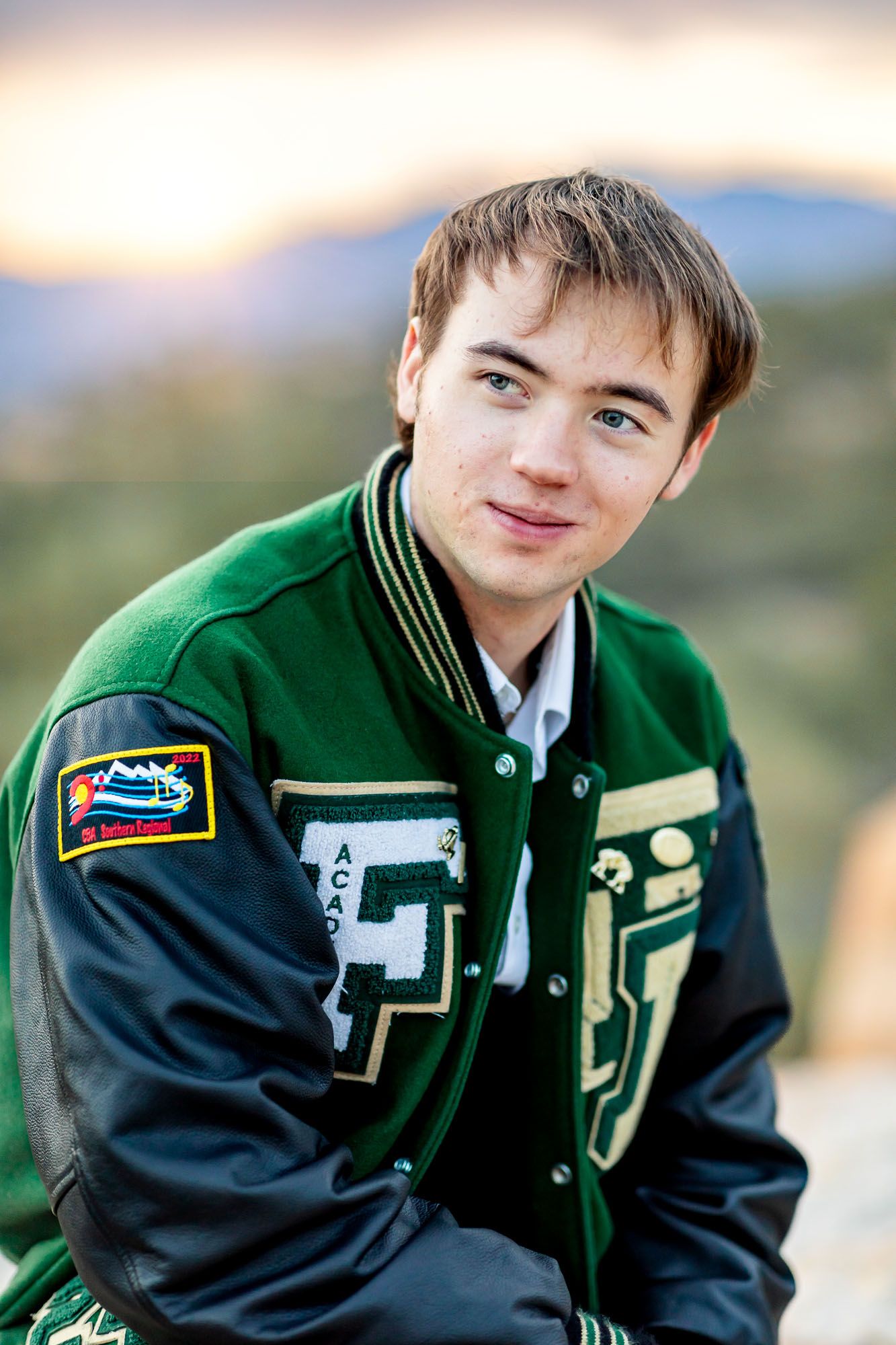 Senior guy sits in letter jacket and grins to the side at his senior session at Palmer Park in Colorado Springs.