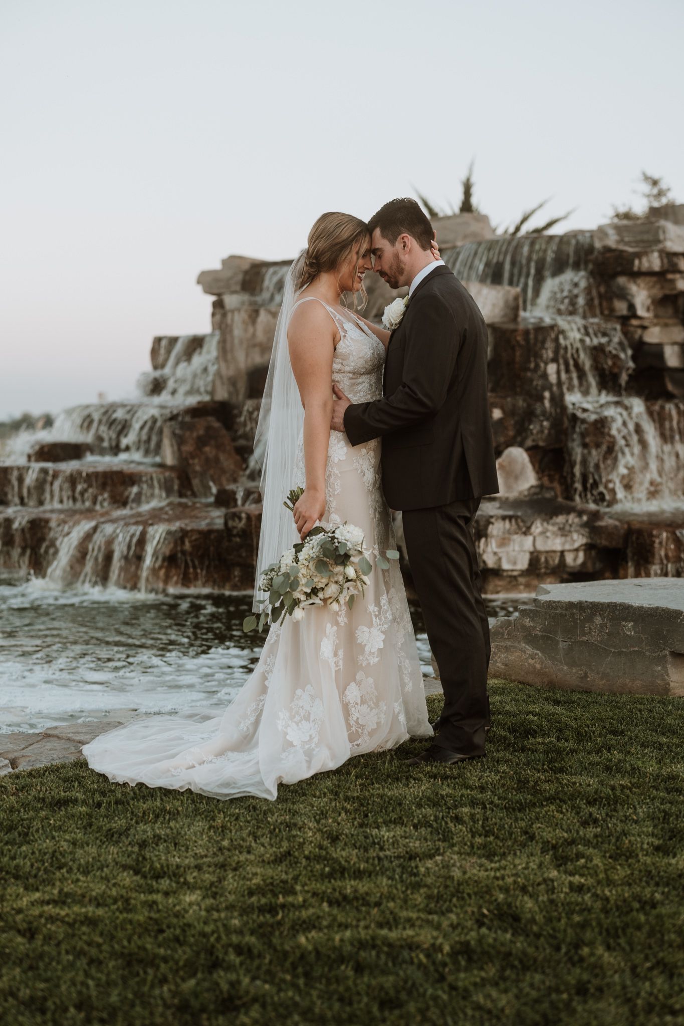 A wedding couple embraces near a cascading waterfall on their special day.