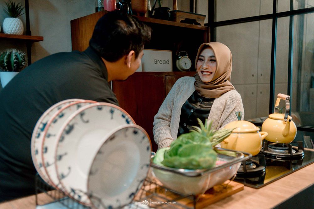 Couple chatting in kitchen with bowl of fresh vegetables and yellow teapot on counter.