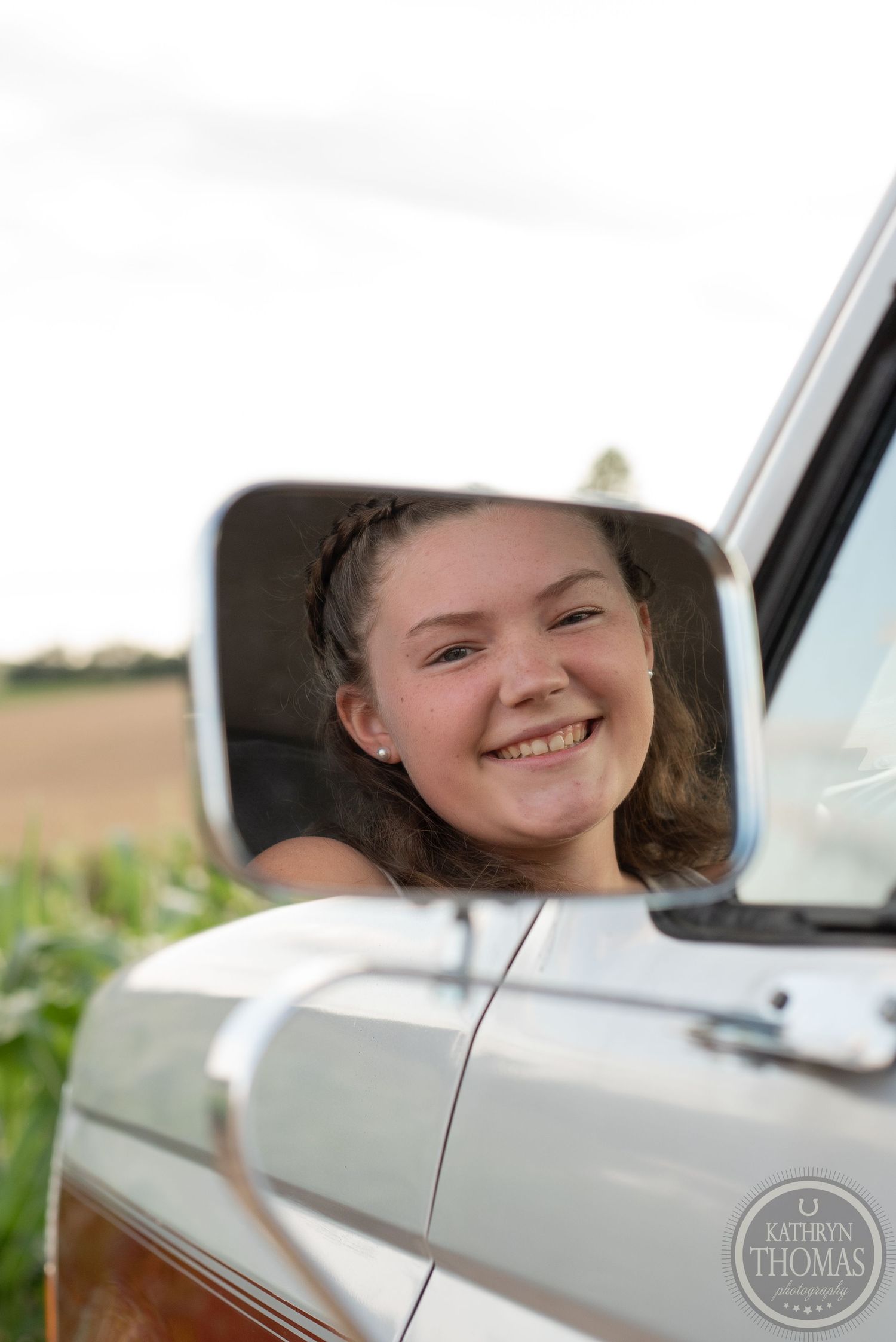 Reflection in side mirror of vintage truck shows joyful expression on sunny rural day.