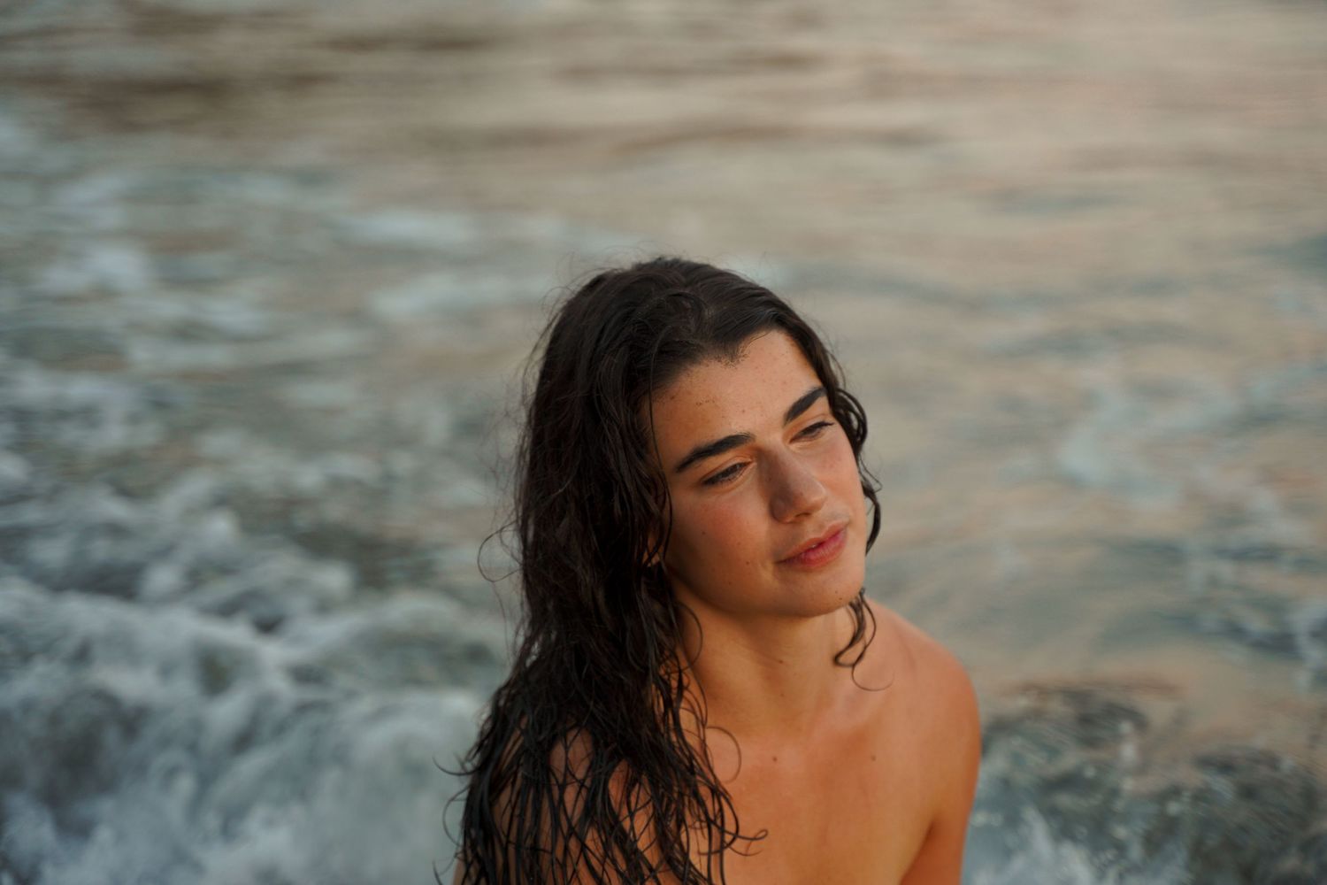 Artistic portrait of woman in water during golden sunset at ocean.