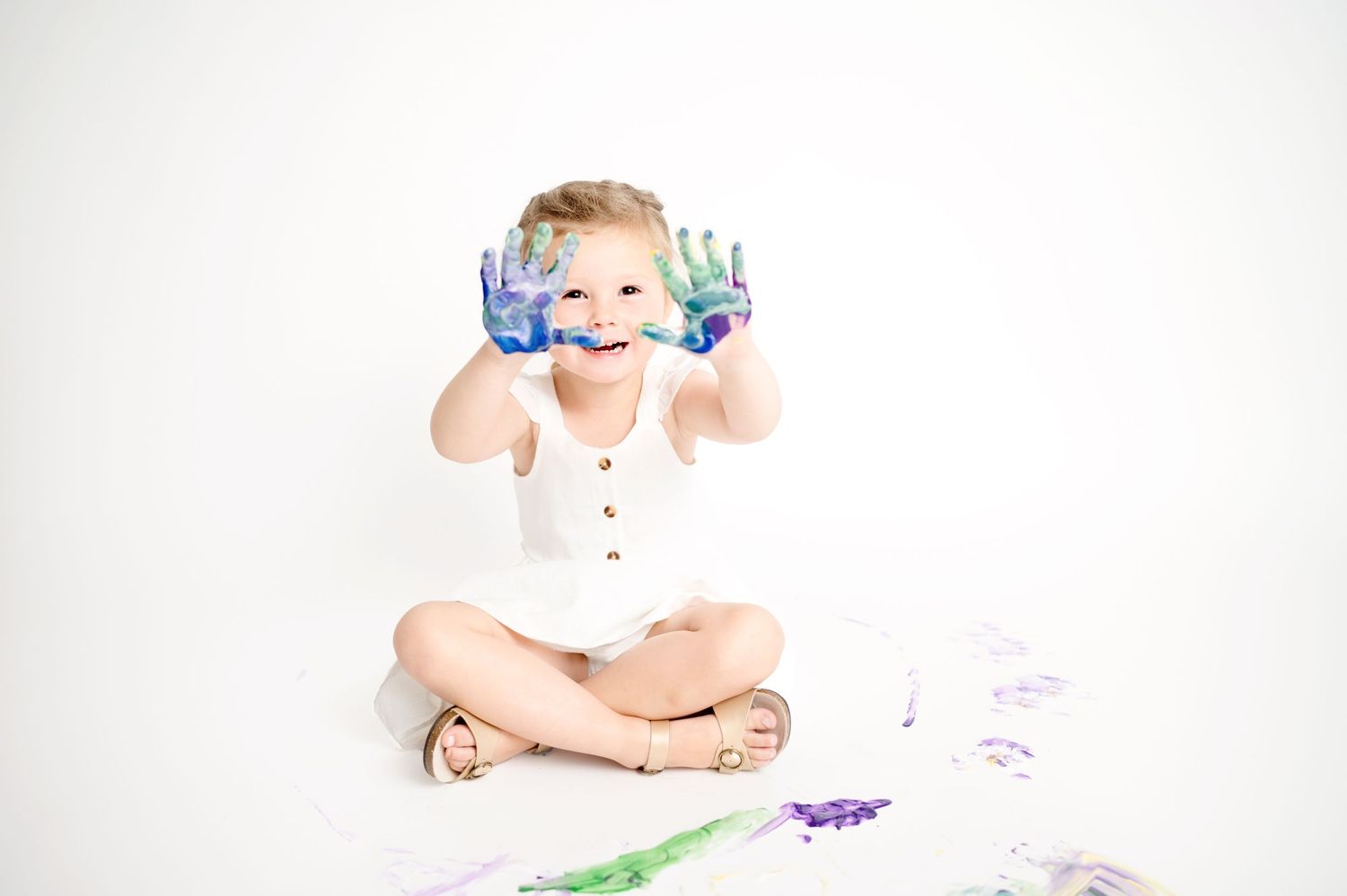Child sitting on floor with colorful paint splatters in white studio setting.
