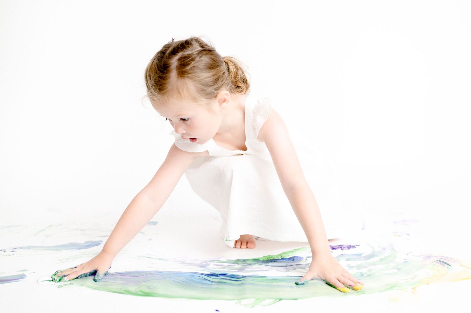People leaning over colorful paint splatter artwork on white floor.