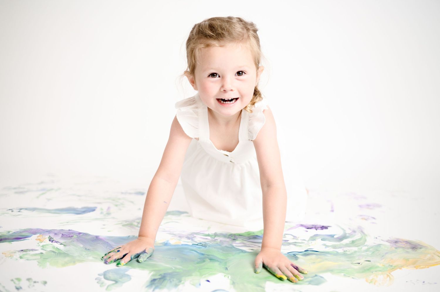 Child plays with colorful paint on white studio floor.