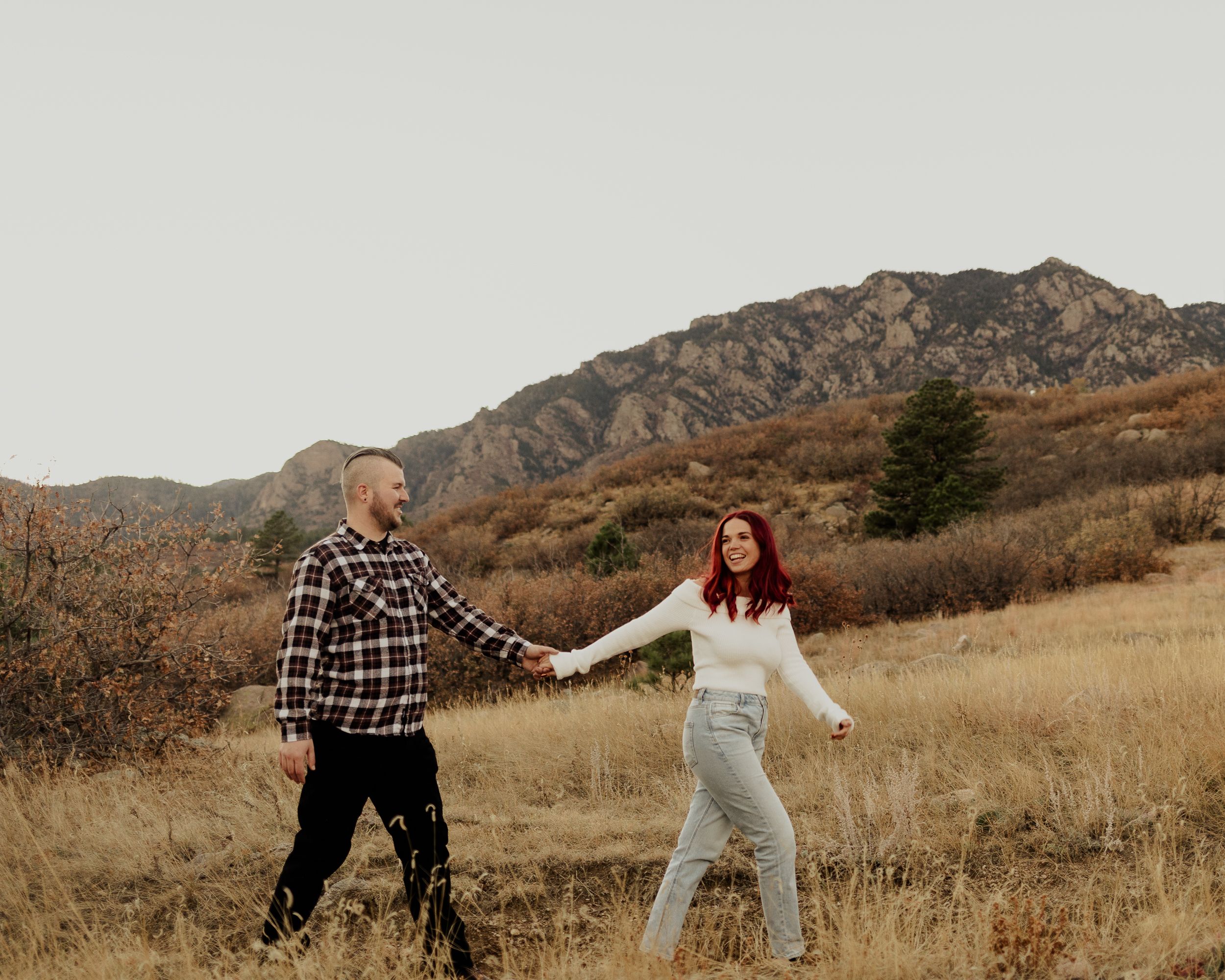 Young couple walks hand in hand with Cheyenne Mountain in the background illuminated with a glowy sunset