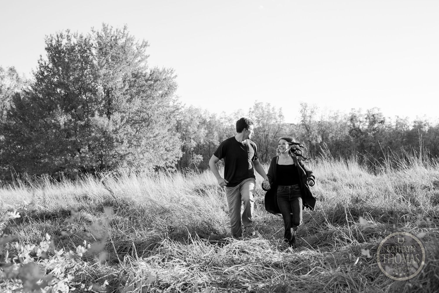 A black and white photograph of two people walking through a meadow on a sunny day.
