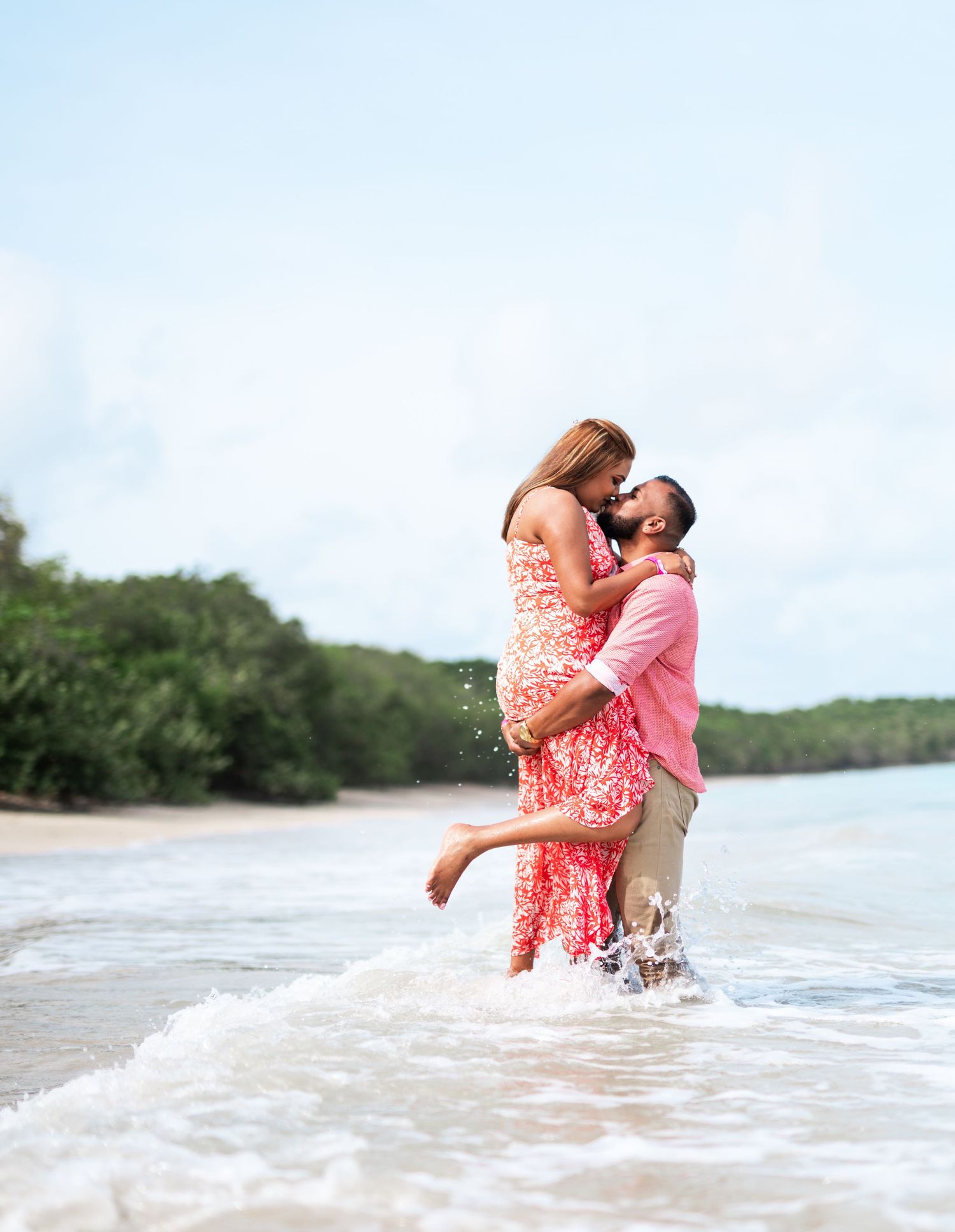 A romantic couple embraces while standing in shallow ocean waters at the beach.