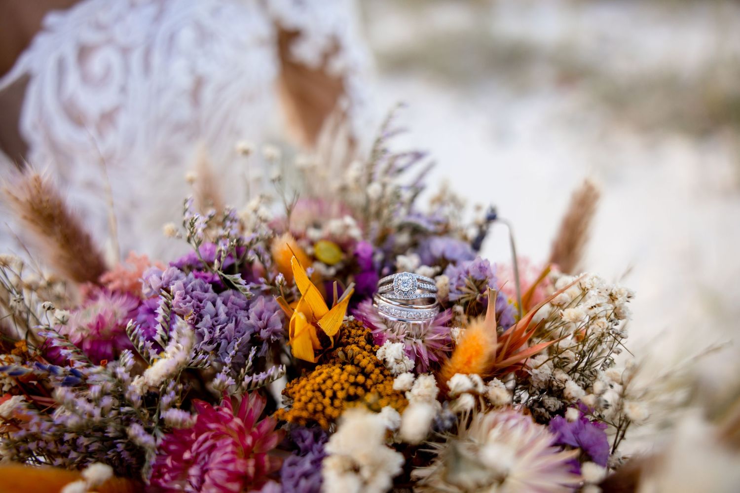 Close-up of a vibrant bohemian bridal bouquet featuring dried purple, orange, and yellow wildflowers with textured greenery.