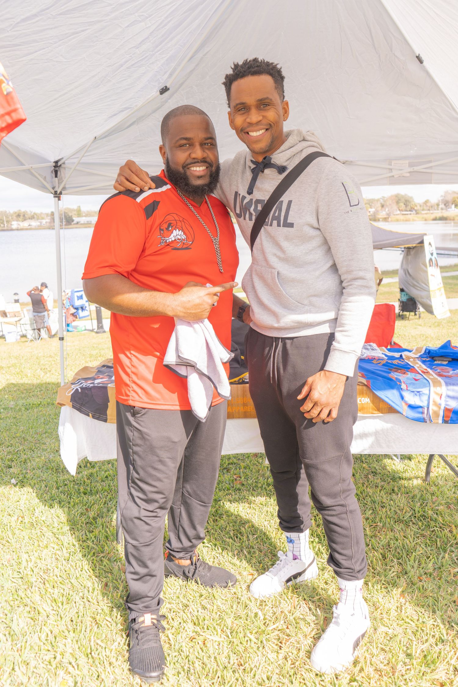 Two attendees pose together under white tent at outdoor community event.