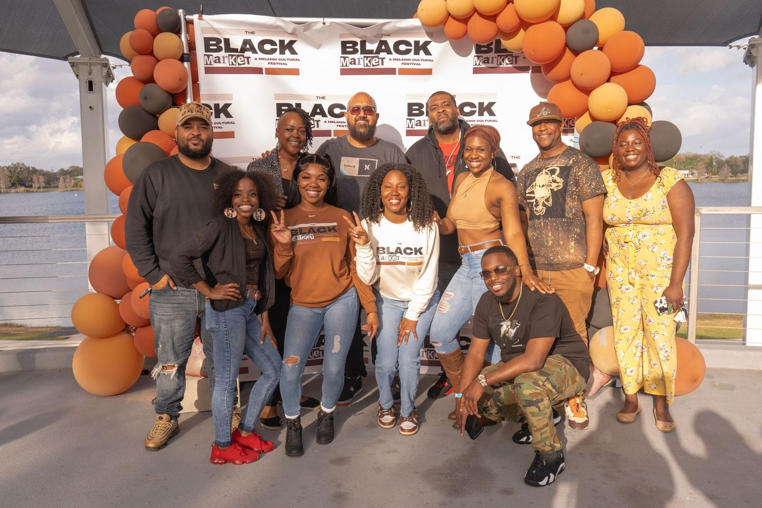 Group photo of event participants with orange balloon decor and branding backdrop.