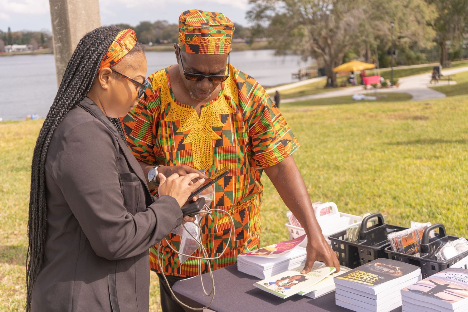 Two vendors discussing products at an outdoor market display table.