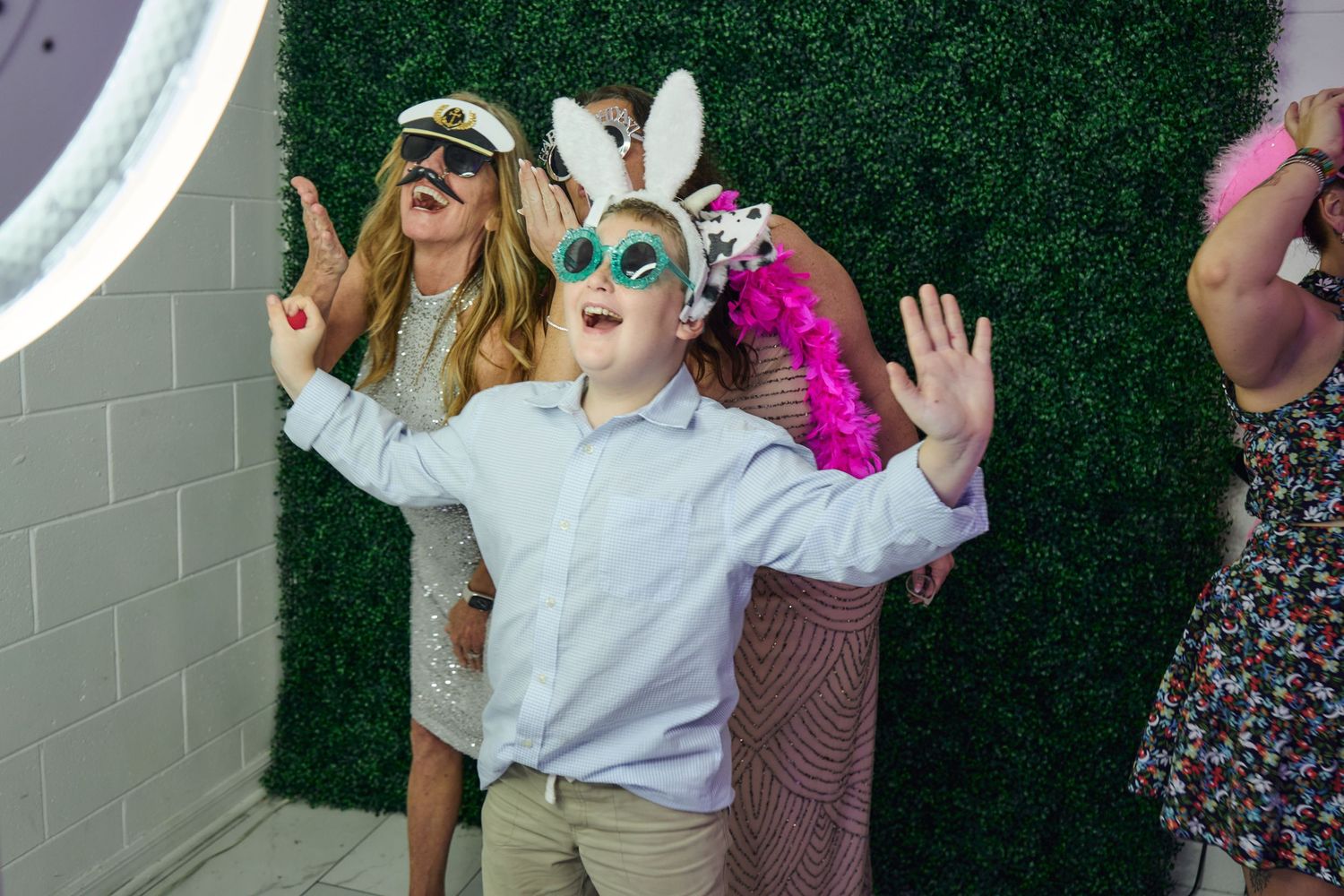Party guests wearing fun masks and costumes posing in front of a green hedge wall.