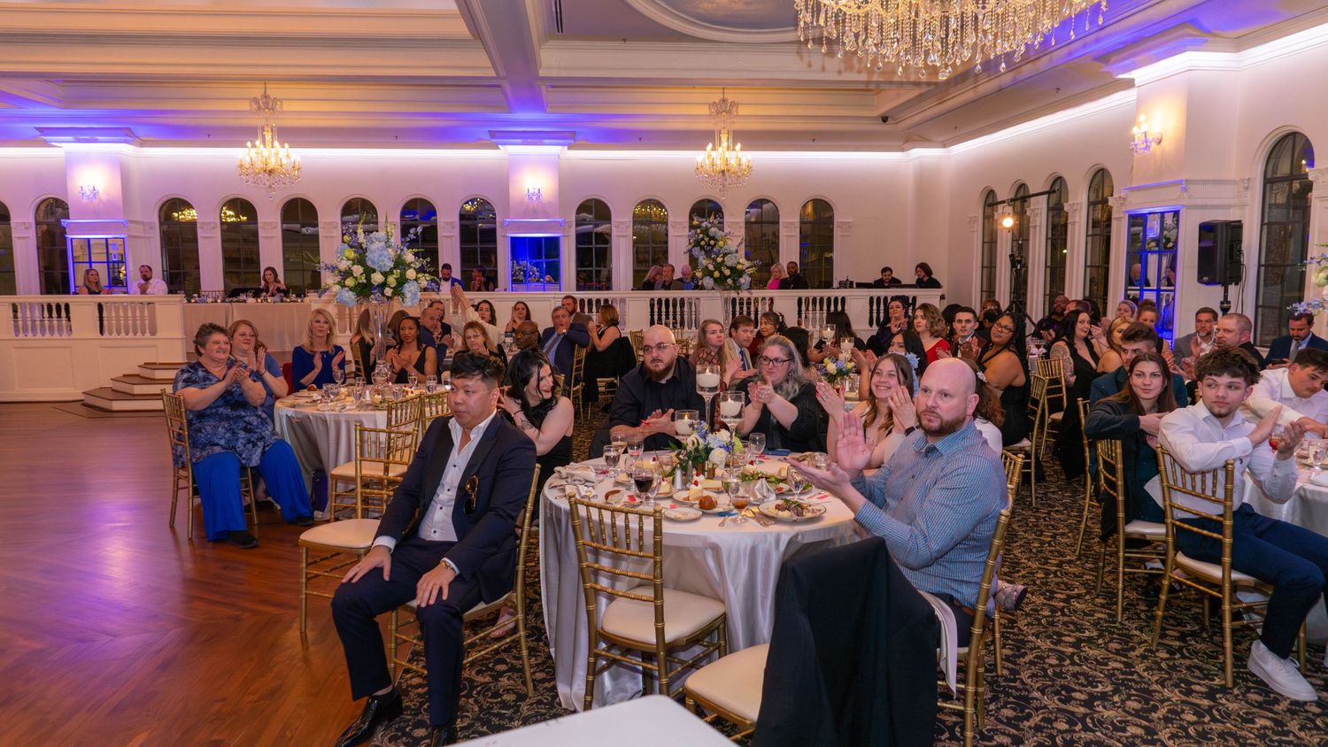 Large banquet hall filled with guests seated at decorated round tables during an evening event.