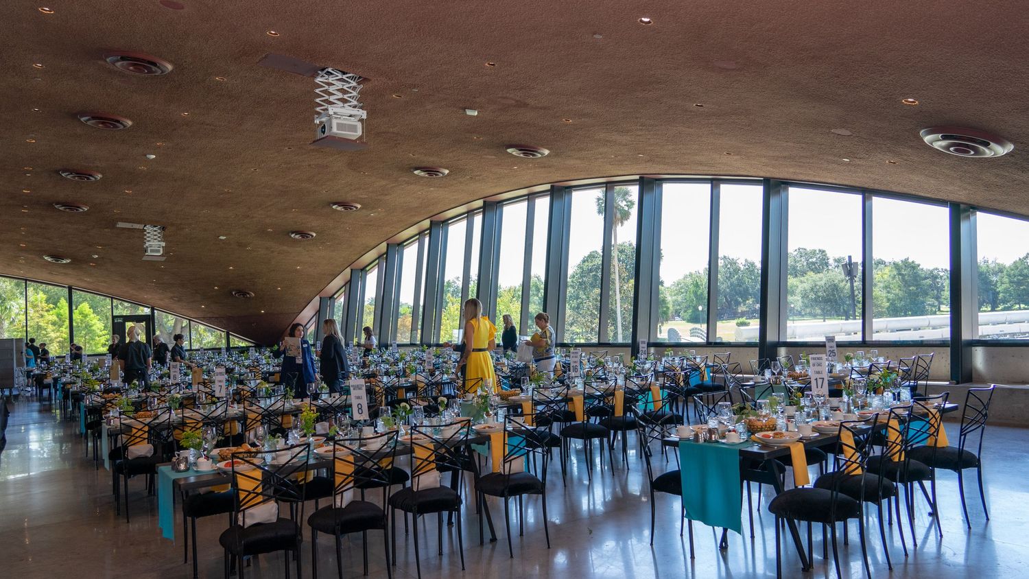 Modern dining hall with curved ceiling, large windows, and multiple tables set up for an event.