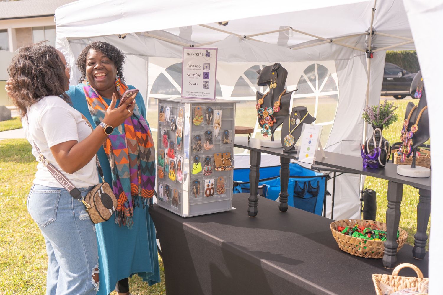 Vendors and customers interacting at a covered market booth with merchandise displays.