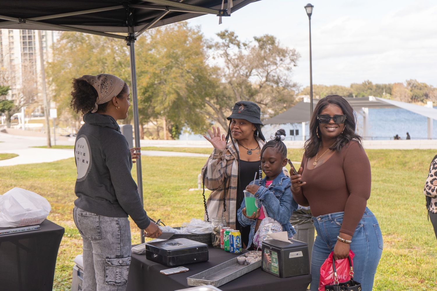 Group chatting near DJ equipment at outdoor event under canopy tent.