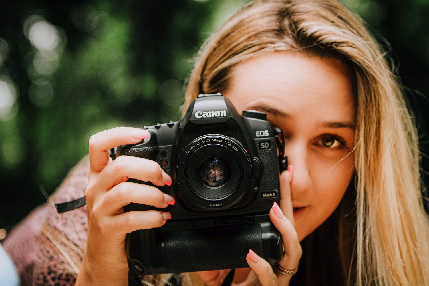 A close-up photograph of someone holding a professional DSLR camera with a blurred green background.