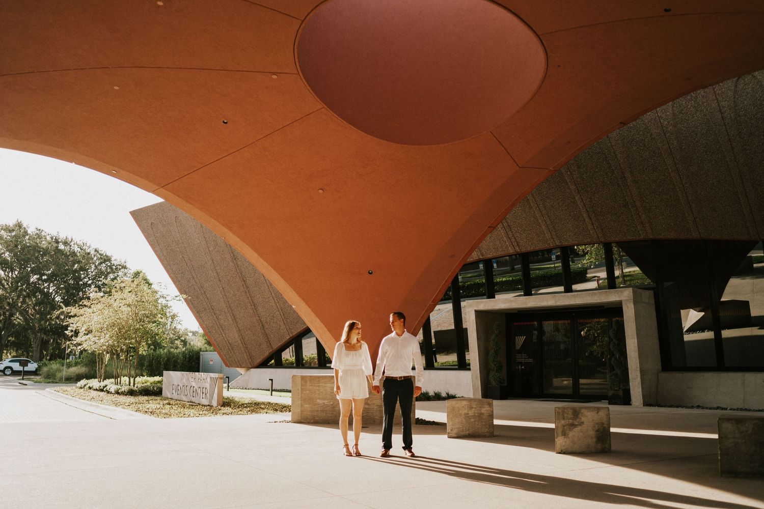 A joyful couple celebrates beneath a geometric architectural structure with palm trees.