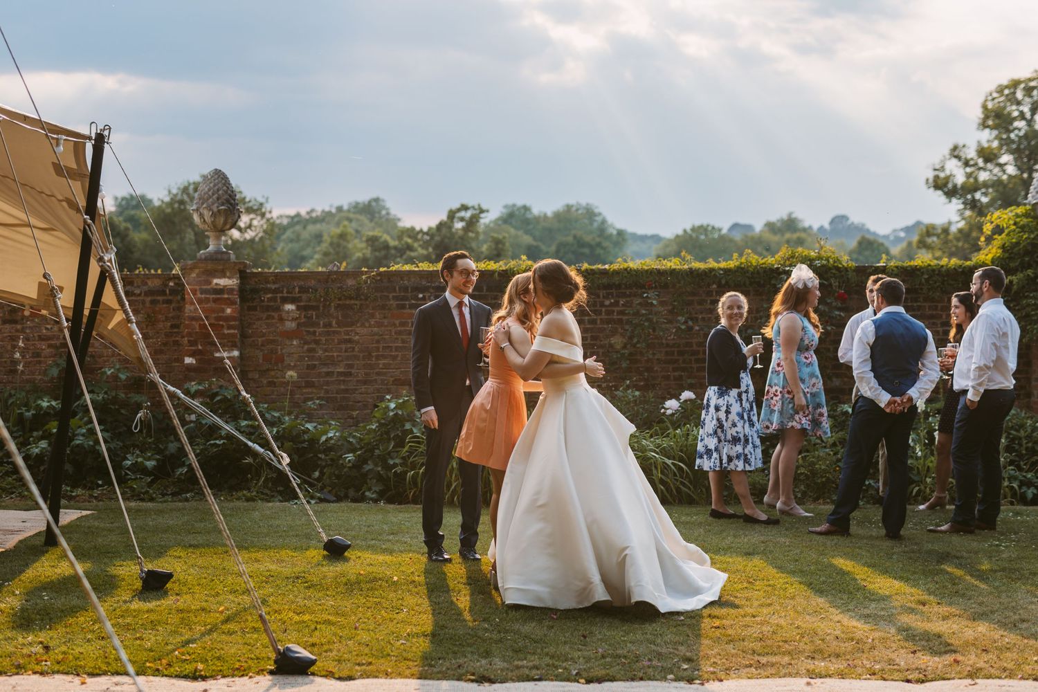 Hot summer evening wedding at Remenham Court Henley on Thames bride hugging guest with sun beams in sky