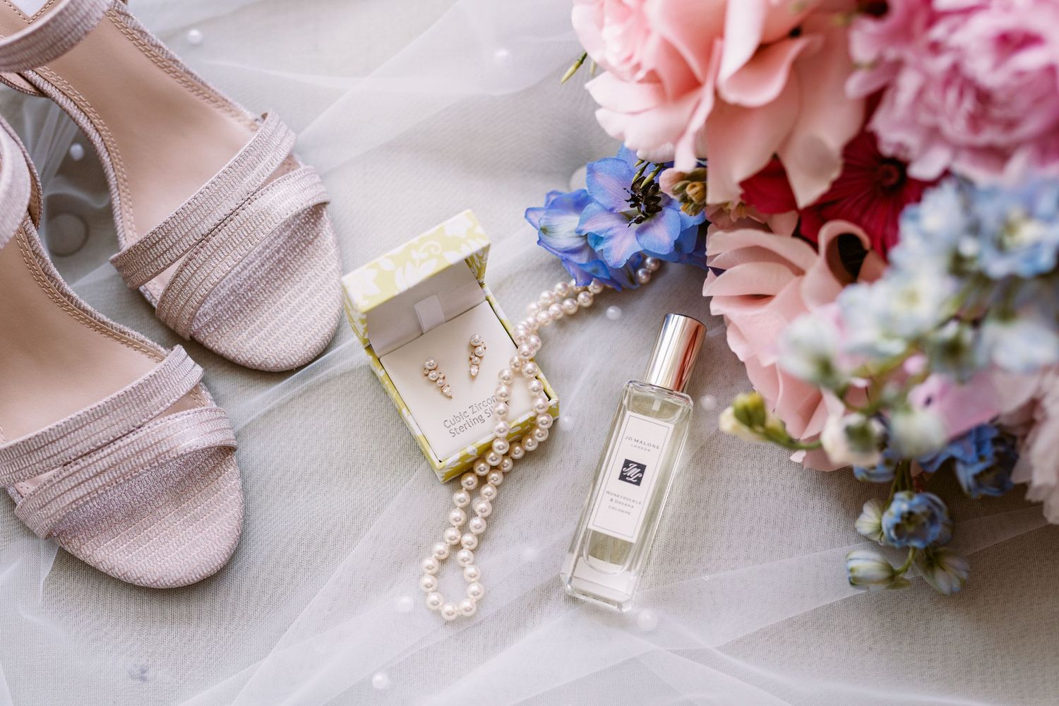 Brides details in flat lay showing perfume jewellery shoes bouquet pretty pinks and blues