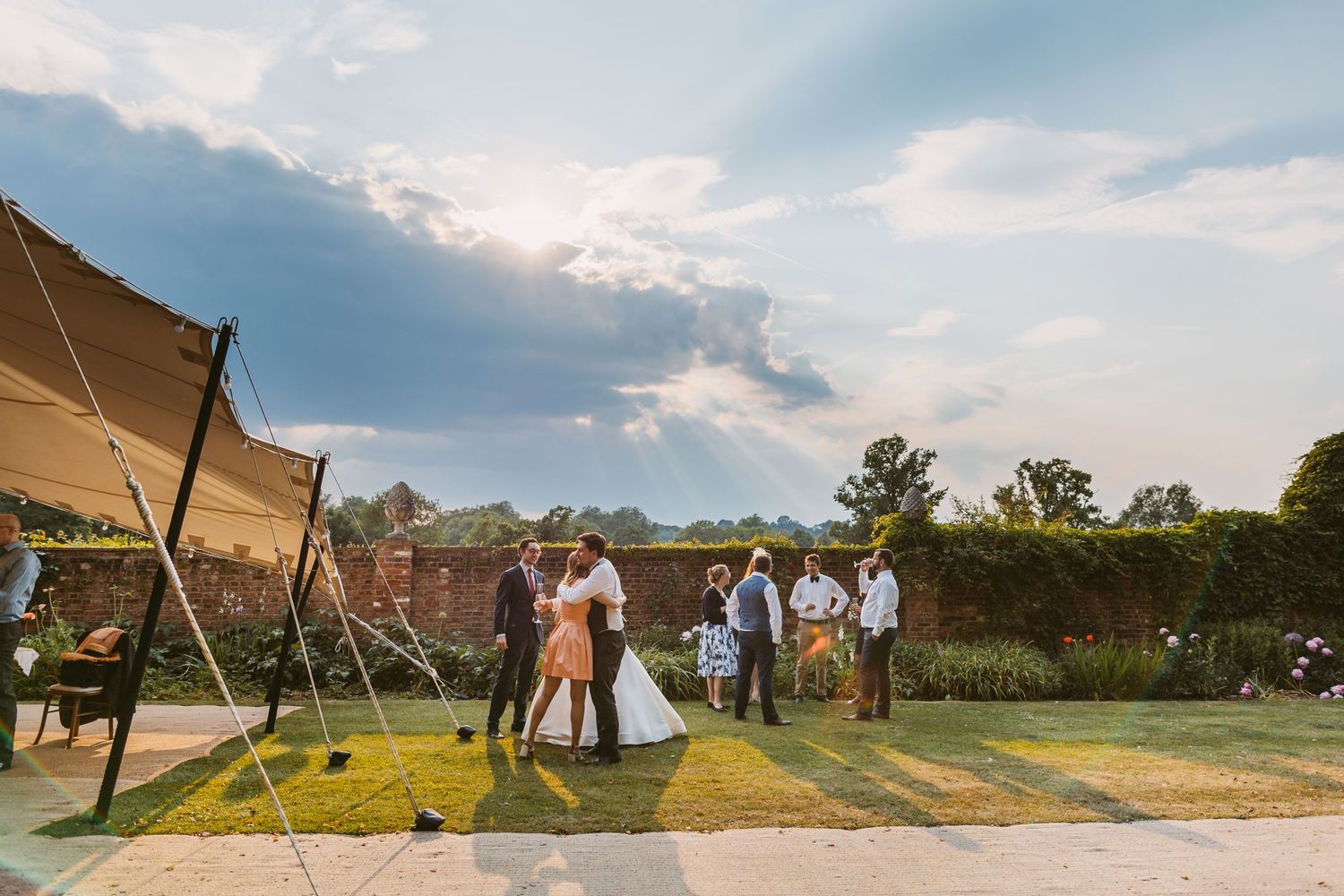 Hot summer evening wedding at Remenham Court Henley on Thames groom hugging guest with sun beams in sky