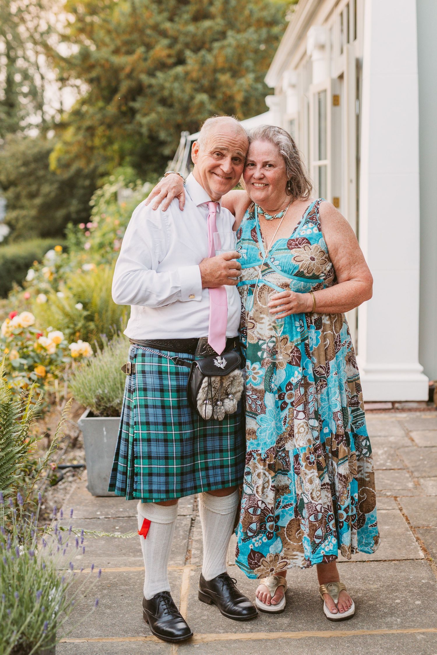 Father of bride wearing kilt hugging his sister on hot summer wedding evening Henley on Thames