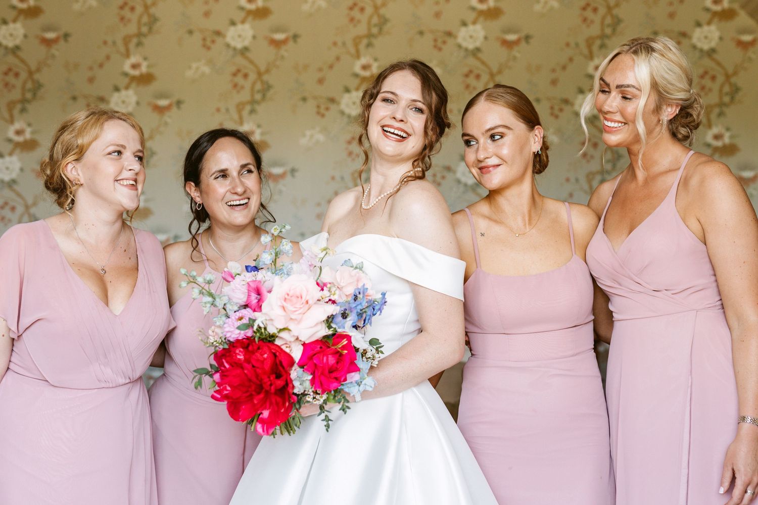 Bride holding her beautiful brightly coloured bouquet surrounded by bridesmaids before the ceremony