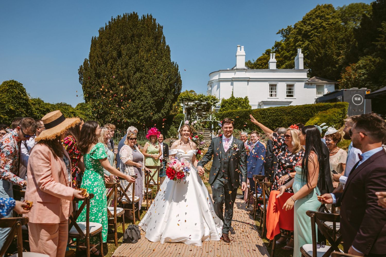 Confetti moment at Incredible wedding venue Remenham Court on hot summers day with blue sky above white house